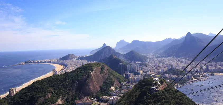 Cabos de aço do bondinho ligando o morro da Urca e parte da cidade e e da praia de Copacabana aparecendo em segundo plano.