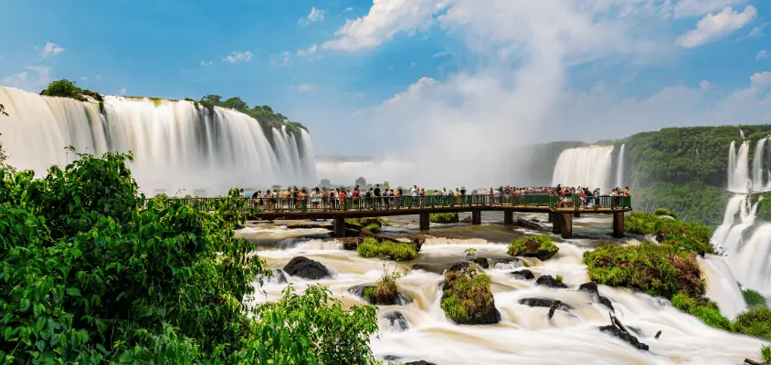 Imagem das cataratas do Iguaçu, com muitos turistas observando da ponte que fica no centro das cataratas.
