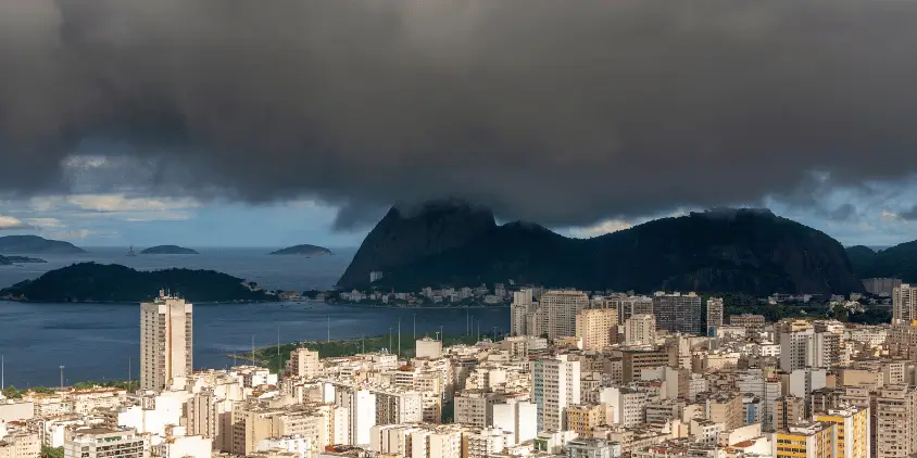 Imagem panorâmica do Rio de Janeiro com o céu fechado. Há uma grande nuvem de chuva na foto.