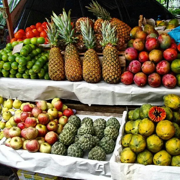Imagem de frutas, como abacaxi, maçã e pera em uma feira de rua.