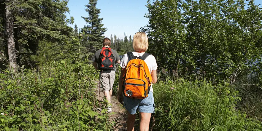 Imagem mostra um casal com mochila nas costas caminhando em uma trilha.