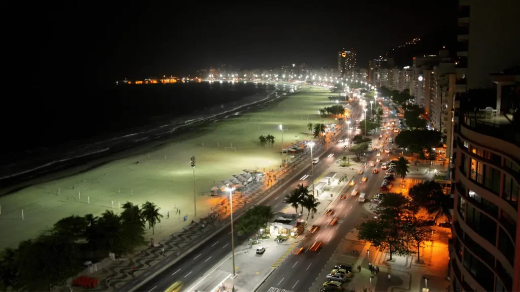 Imagem noturna da avenida Atlântica toda iluminada, com a praia de copacabana