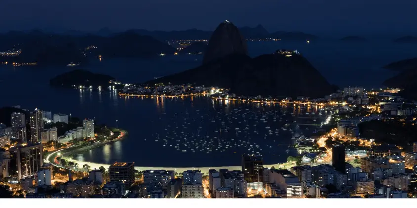 Imagem aérea do Rio de Janeiro de noite, mostrando a Baía de Guanabara e o Pão de Açúcar