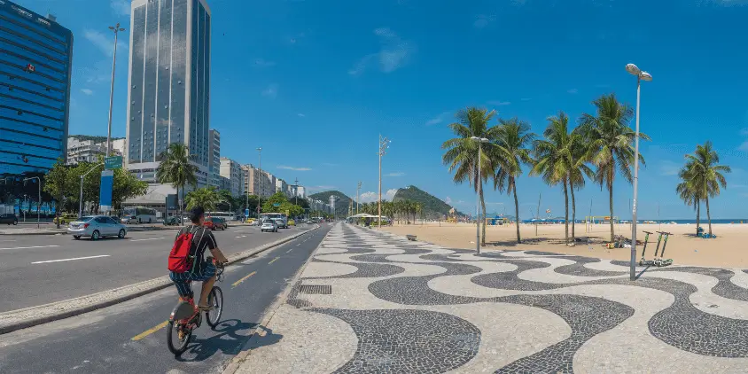 Imagem do calçadão de copacabana, com um homem andando de bicicleta na ciclovia